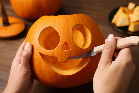 Woman carving pumpkin for Halloween at wooden table, closeupの写真素材