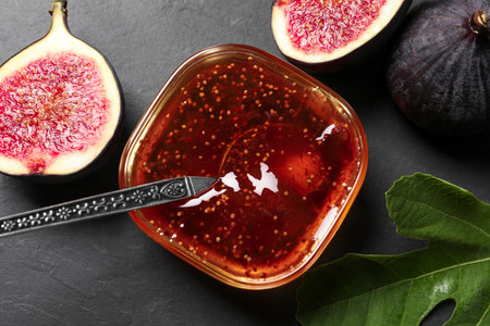 Glass bowl with tasty sweet jam, spoon, fresh figs and green leaf on gray table, flat layの写真素材
