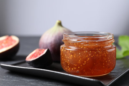 Jar of tasty fig jam and fresh fruits on black table, closeup. Space for textの写真素材