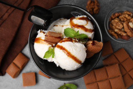 Bowl of tasty ice cream with caramel sauce, candies and mint on brown table, flat layの写真素材