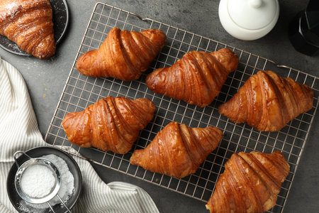 Delicious fresh croissants with powdered sugar on gray table, flat lay