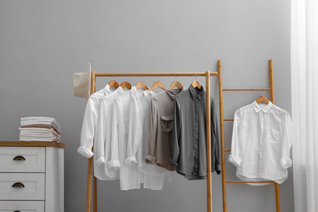 Rack with different stylish shirts, hat and chest of drawers near gray wall indoors. Organizing clothesの写真素材