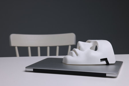 Mask and laptop on white table against gray background