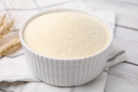 Uncooked organic semolina in bowl and spikelets on white wooden table, closeupの写真素材