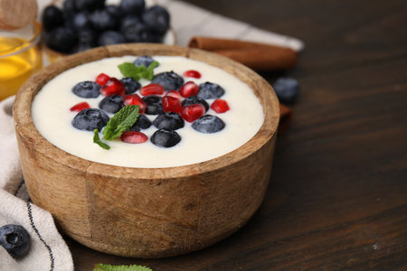 Bowl of delicious semolina pudding with blueberries, pomegranate and mint on wooden table, closeup. Space for textの写真素材