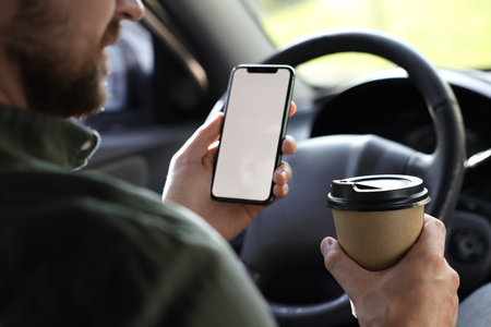 Coffee to go. Man with paper cup of drink and smartphone in car, closeupの写真素材