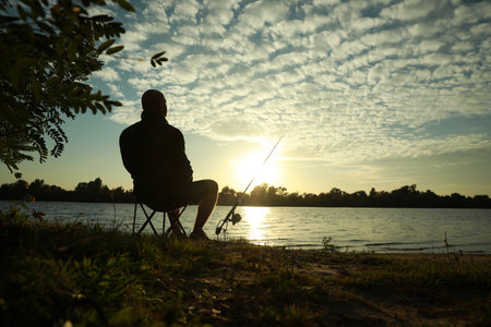 Fisherman with rod sitting on folding chair and fishing at riverside, space for textの写真素材