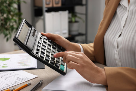 Woman using calculator at table in office, closeup