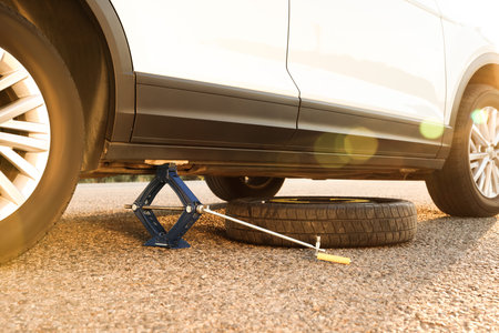 Car lifted by scissor jack and spare wheel on roadsideの写真素材