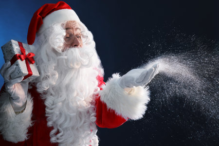 Santa Claus with Christmas gift blowing snow on dark blue backgroundの写真素材