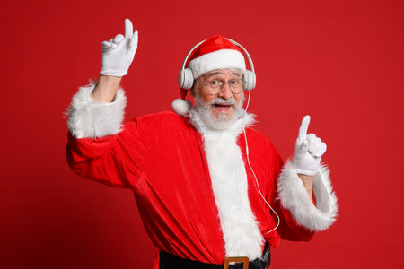 Merry Christmas. Santa Claus in headphones listening to music on red backgroundの写真素材