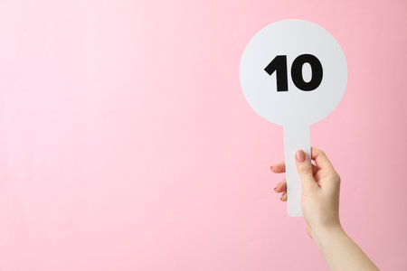 Woman holding auction paddle with number 10 on pink background, closeup. Space for textの写真素材