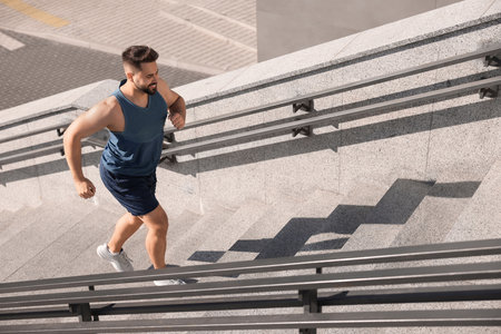 Smiling man running up stairs outdoors on sunny day. Space for textの写真素材