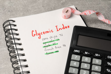 Glycemic Index. Notebook with information, measuring tape and calculator on light gray table, closeupの写真素材