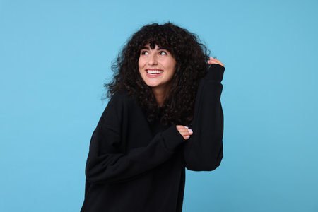 Happy young woman in stylish black sweater on light blue background