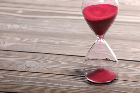 Hourglass with pink flowing sand on wooden table. Space for textの写真素材