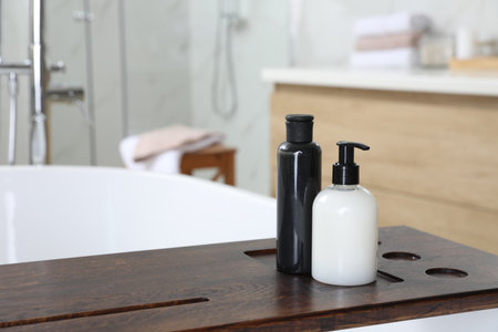 Wooden bath tray with bottles of shower gels on tub indoors, space for textの写真素材