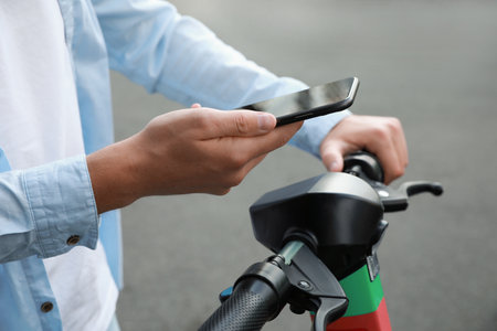 Man using smartphone to pay and unblock electric kick scooter outdoors, closeupの写真素材