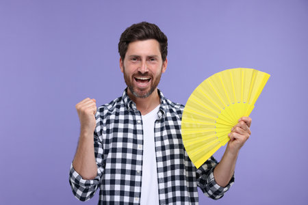 Happy man holding hand fan on purple backgroundの写真素材