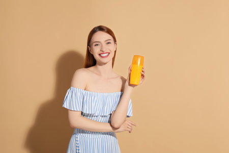 Beautiful young woman holding sun protection cream on beige background, space for textの写真素材
