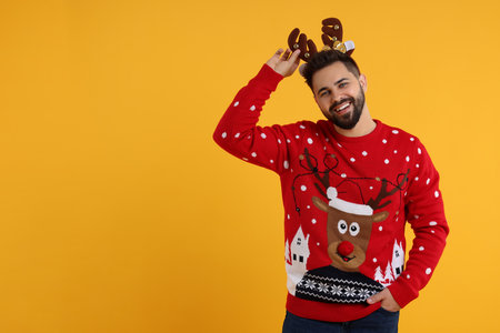 Happy young man in Christmas sweater and reindeer headband on orange background. Space for textの写真素材