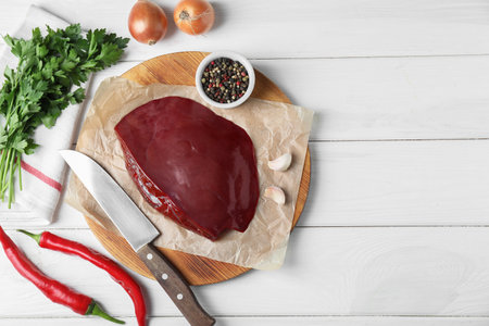 Piece of raw beef liver, knife and products on white wooden table, flat lay. Space for textの写真素材