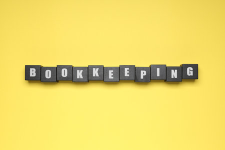 Word Bookkeeping made with black cubes on yellow background, top viewの写真素材