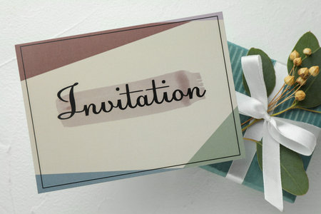 Beautiful card with word Invitation, eucalyptus leaves and gift box on white table, flat layの写真素材