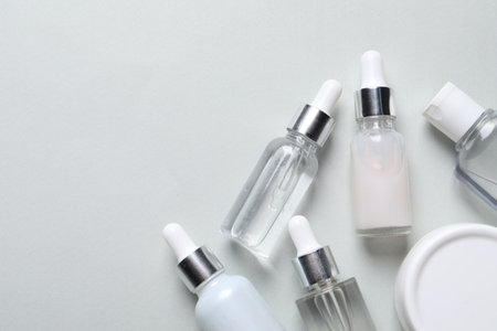 Many bottles of cosmetic serum on light gray background, flat lay. Space for textの写真素材