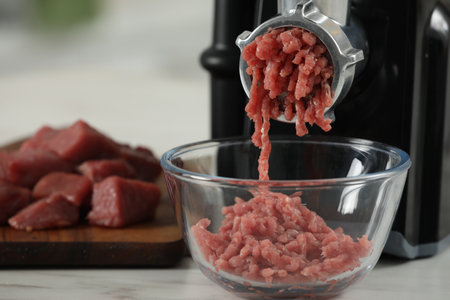 Electric meat grinder with beef mince on white table against blurred background, selective focus. Space for textの写真素材