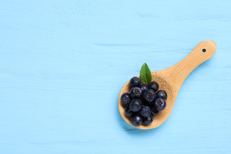 Spoon with ripe bilberries and leaf on light blue wooden table, top view. Space for textの写真素材