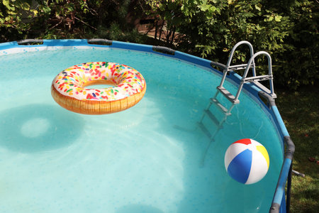 Inflatable ring and ball floating on water in above ground swimming pool outdoorsの写真素材