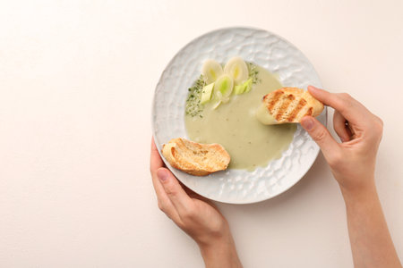 Woman dipping crouton into delicious leek soup at light table, top view. Space for textの写真素材