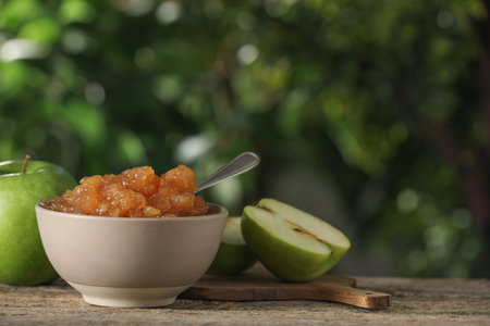 Bowl with delicious apple jam and fresh fruits on wooden table against blurred background, space for textの写真素材