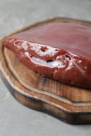 Piece of raw beef liver on gray table, closeup