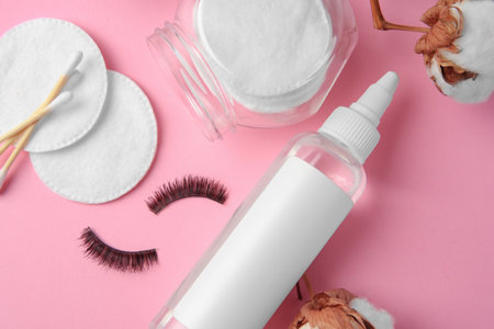 Bottle of makeup remover, cotton flowers, pads, swabs and false eyelashes on pink background, flat layの写真素材