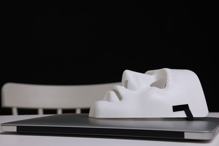 Mask and laptop on white table against black background, closeupの写真素材