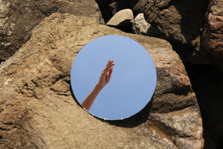 Round mirror reflecting woman's hand on stones on sunny day, closeupの写真素材
