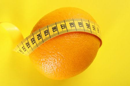 Cellulite problem. Orange with measuring tape on yellow background, top viewの写真素材