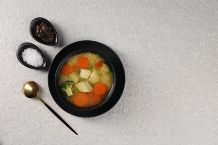 Tasty chicken soup with noodles and vegetables in bowl served on light textured table, flat lay....