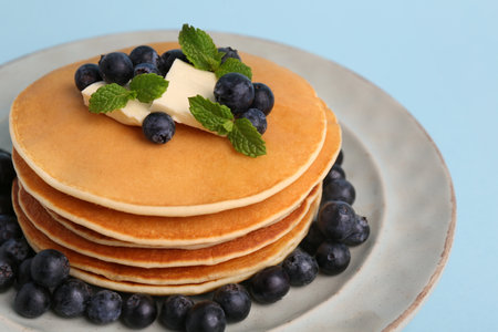 Stack of tasty pancakes with blueberries, butter and mint on light blue background, closeupの写真素材