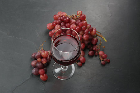 Delicious fresh red grapes and glass of wine on black table, above view