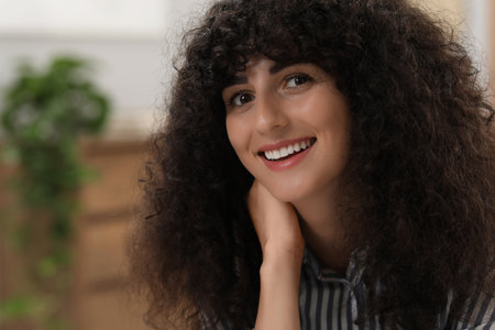Portrait of beautiful woman with curly hair indoors. Attractive lady smiling and posing for camera. Space for textの写真素材
