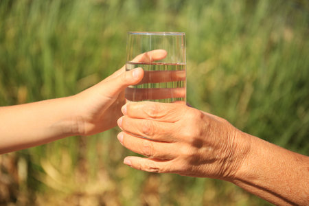 Child giving glass of water to elderly woman outdoors on sunny day, closeupの写真素材