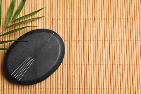 Acupuncture needles, spa stone and leaf on bamboo mat, flat lay. Space for textの写真素材