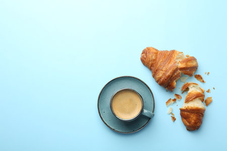 Delicious fresh croissant and cup of coffee on light blue background, flat lay. Space for textの写真素材