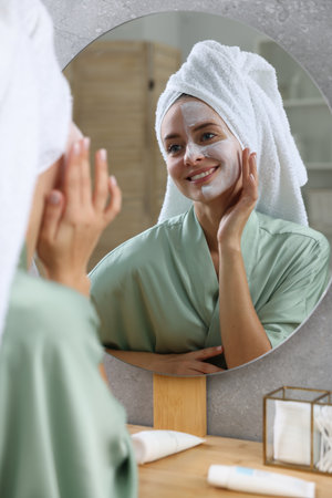 Woman with face mask near mirror in bathroom. Spa treatmentsの写真素材