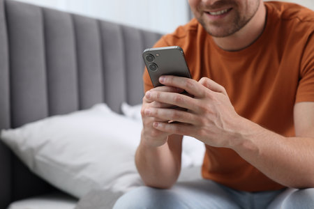 Man sending message via smartphone on bed at home, closeup. Space for textの写真素材