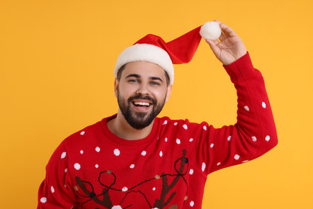 Happy young man in Christmas sweater and Santa hat on orange backgroundの写真素材