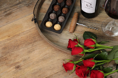 Red wine, chocolate truffles, corkscrew and roses on wooden table, above view. Space for textの写真素材